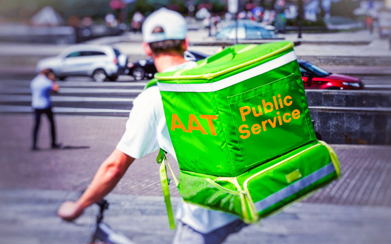 Photo of man on bike carrying green box on his back with the words "AAT Public Service"